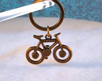 May include: A bronze-colored bicycle keychain with a key ring. The bicycle is detailed with a chain and spokes.