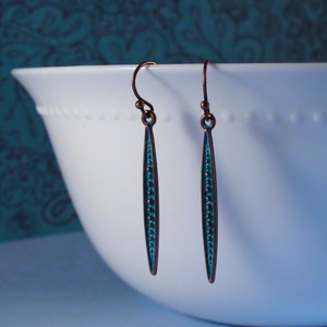 May include: A pair of long, thin, turquoise blue earrings with copper wire and a beaded design.