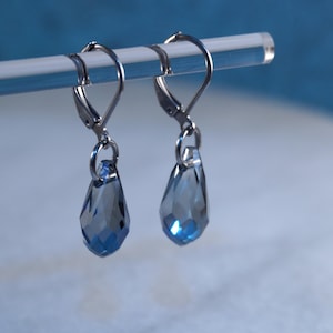 May include: A pair of silver dangle earrings with teardrop-shaped blue crystal accents.