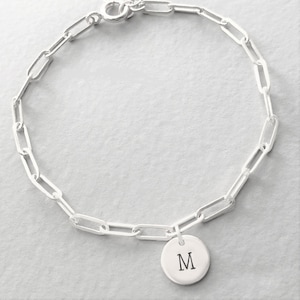 May include: A silver chain bracelet with a silver charm that has the letter "M" engraved on it.