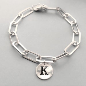 May include: A silver chain bracelet with a silver charm featuring the letter K.