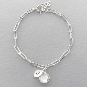 May include: A silver chain bracelet with a clear crystal charm and a silver leaf charm with the letter 'J' engraved on it.