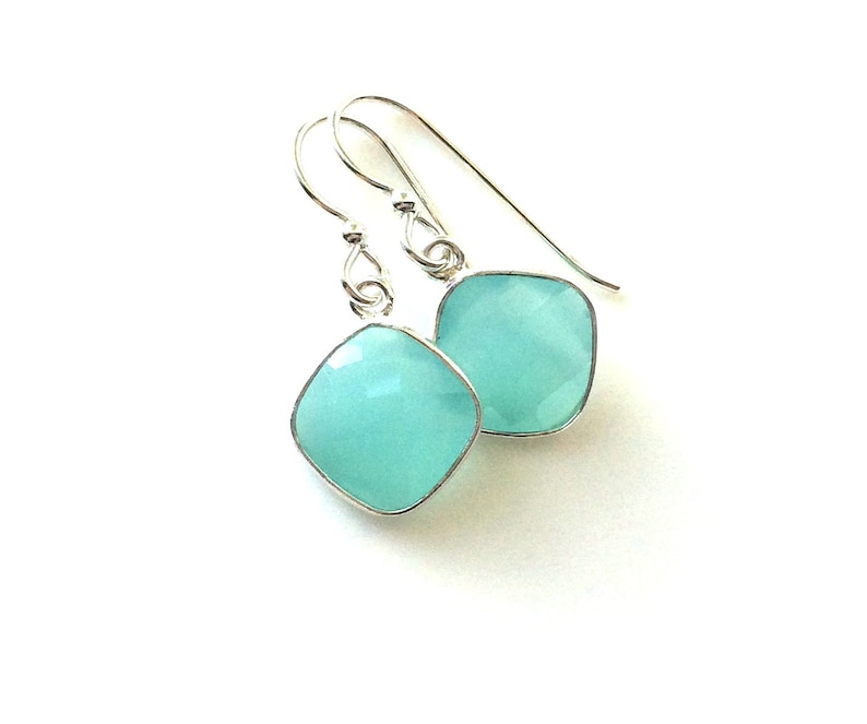 May include: A pair of silver dangle earrings with light blue square-shaped gemstones.