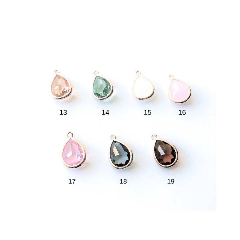 May include: Nine teardrop-shaped glass charms with gold-tone metal settings. The charms are in various colors, including pink, green, white, and gray.