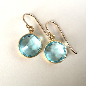 May include: A pair of gold earrings with light blue round gemstone drops.