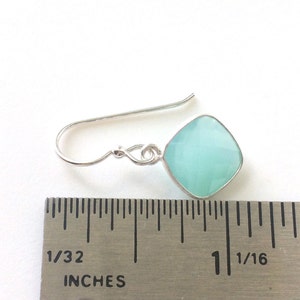 May include: Silver dangle earrings with a light blue square gemstone. The earrings are measured against a ruler, showing the gemstone is about 1 inch wide.