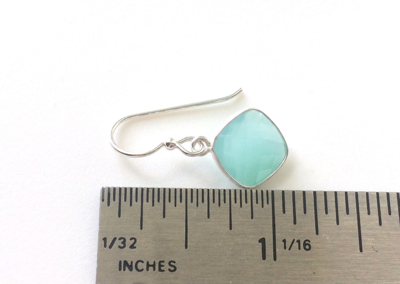 May include: Silver dangle earrings with a light blue square gemstone. The earrings are measured against a ruler, showing the gemstone is about 1 inch wide.