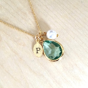 May include: Gold necklace with a teardrop-shaped green gemstone, a small pearl, and a leaf charm with the letter "P" engraved on it.