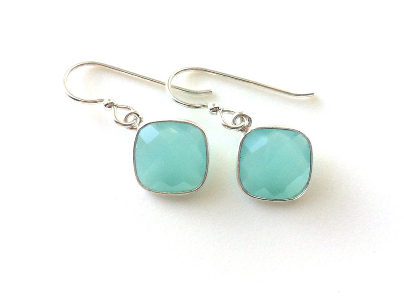 May include: A pair of silver earrings with light blue square-shaped gemstones.