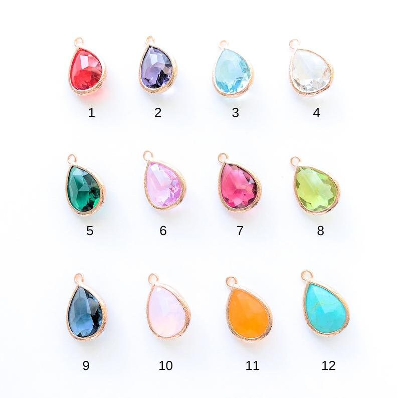 May include: Twelve teardrop-shaped glass charms in various colors, including red, purple, blue, green, pink, orange, and turquoise. Each charm has a gold-colored metal bail.