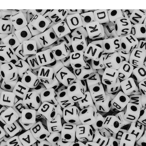 Puede incluir: Una imagen de primer plano de un montón de cuentas de letras de plástico blanco. Las cuentas son todas letras diferentes del alfabeto y están dispuestas en un orden aleatorio.