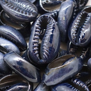 Könnte beinhalten: Nahaufnahme eines Stapels blauer Kaurischnecken. Die Muscheln sind glatt und glänzend, in einem dunklen Blau.