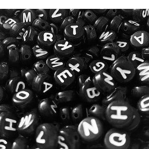 May include: A monochrome image showing a collection of black, spherical beads. Each bead features a white letter from the English alphabet. The beads are piled together, creating a textured surface.