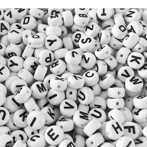 Puede incluir: Un montón grande de cuentas de letras de plástico blanco con letras negras. Las cuentas son todas redondas y tienen un agujero en el centro. Las letras son todas en mayúsculas e incluyen las letras A a la Z.