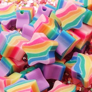 Puede incluir: Primer plano de coloridas cuentas de estrella y cuadradas de arcoíris. Las cuentas están hechas de un material liso, similar al plástico, y tienen un patrón de remolino.