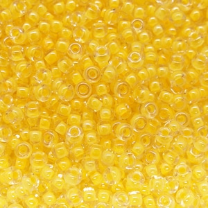 May include: A close-up of a large quantity of small, translucent yellow beads. The beads are round with a small hole in the center.