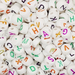 Könnte beinhalten: Nahaufnahme von weißen Kunststoffbuchstabenperlen mit bunten Buchstaben. Die Buchstaben umfassen A, B, C, D, E, F, G, H, I, J, K, L, M, N, O, P, Q, R, S, T, U, V, W, X, Y und Z.