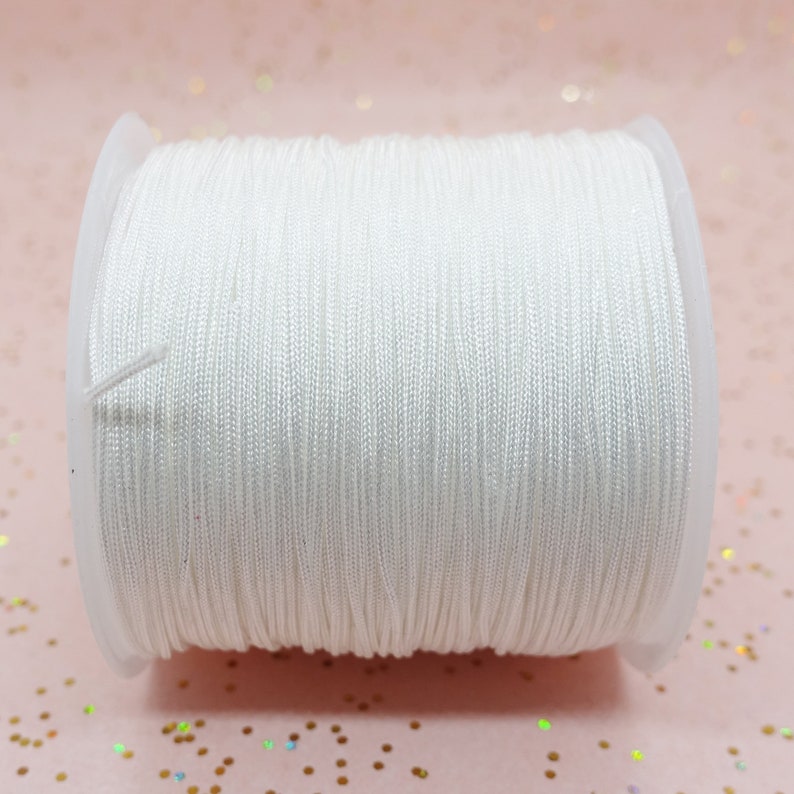 Pode incluir: Um carretel de cord&atilde;o el&aacute;stico branco. O cord&atilde;o &eacute; enrolado firmemente em torno de um carretel de pl&aacute;stico transparente. O el&aacute;stico &eacute; de cor branca brilhante. O fundo &eacute; rosa claro. Ideal para artesanato.