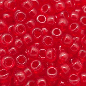 Könnte beinhalten: Nahaufnahme eines Stapels kleiner, runder, roter Saatperlen. Die Perlen sind durchscheinend und haben eine glänzende Oberfläche.