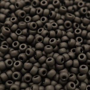 May include: A close-up image of a pile of small, round, dark brown beads. The beads have a matte finish and are all the same size.