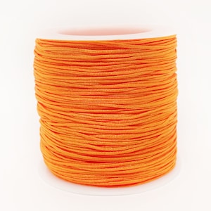 May include: A spool of bright orange nylon cord. The cord is tightly wound around a white plastic core. The colour is a vibrant, solid orange, and the cord appears smooth and uniform in texture. Suitable for crafts and jewellery making.