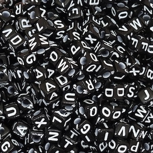 Könnte beinhalten: Ein Nahaufnahmebild eines großen Haufens schwarzer Buchstabenperlen. Die Perlen sind aus Kunststoff und haben weiße Buchstaben darauf. Die Buchstaben sind alle unterschiedlich und zufällig angeordnet.