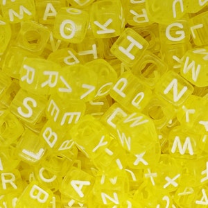 Può includere: Un'immagine ravvicinata di un mucchio di perline di plastica gialle a forma di lettere. Le perline sono tutte lettere diverse dell'alfabeto.