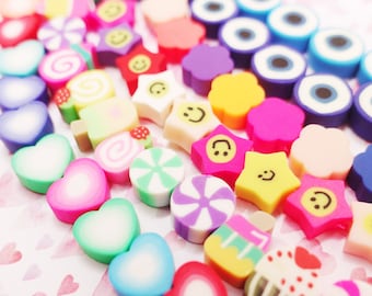 Könnte beinhalten: Sortiment an bunten Polymer Clay Charms in verschiedenen Formen, darunter Herzen, Sterne, Wirbel und Smiley-Gesichter. Die Charms sind perfekt für die Schmuckherstellung, das Scrapbooking und andere Bastelprojekte.