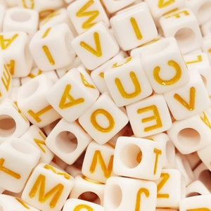 Può includere: Primo piano di un mucchio di perline di lettere di plastica bianca con lettere gialle. Le lettere includono A, B, C, D, E, F, G, H, I, J, K, L, M, N, O, P, Q, R, S, T, U, V, W, X, Y e Z.