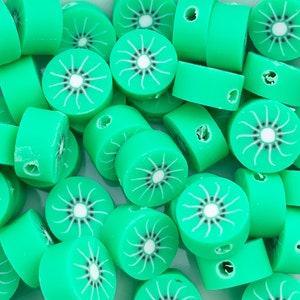 Könnte beinhalten: Eine Ansammlung hellgrüner Polymer Clay Perlen, jede in Form einer Kiwi-Scheibe. Die Perlen haben einen zentralen weißen Kreis mit schwarzen Samen und weißen Strahlen. Die Perlen sind zylindrisch mit einem Loch zum Auffädeln.