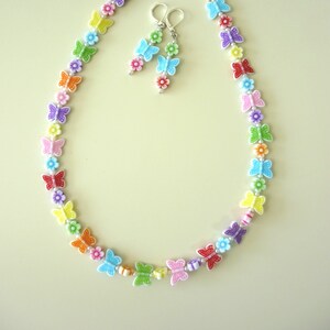 May include: A rainbow-colored necklace and earrings set featuring butterfly and flower charms. The necklace is made of plastic beads and has a silver chain closure. The earrings are dangle style with a butterfly charm at the bottom.