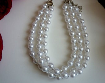 Puede incluir: Un collar de perlas de tres hileras con cierres plateados. El collar está hecho de perlas falsas blancas.