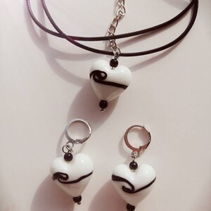 Puede incluir: Un collar de cord&oacute;n negro con un colgante de coraz&oacute;n blanco con un dise&ntilde;o de espiral negro. Pendientes a juego con colgantes de coraz&oacute;n blanco y dise&ntilde;os de espiral negro.