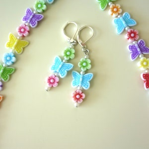 May include: A rainbow colored necklace and matching earrings with butterfly and flower charms. The necklace and earrings are made of plastic and metal.