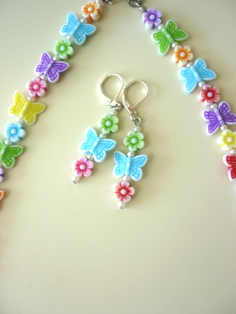 May include: A rainbow colored necklace and matching earrings with butterfly and flower charms. The necklace and earrings are made of plastic and metal.