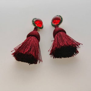 May include: A pair of maroon tassel earrings with red and green gem accents.