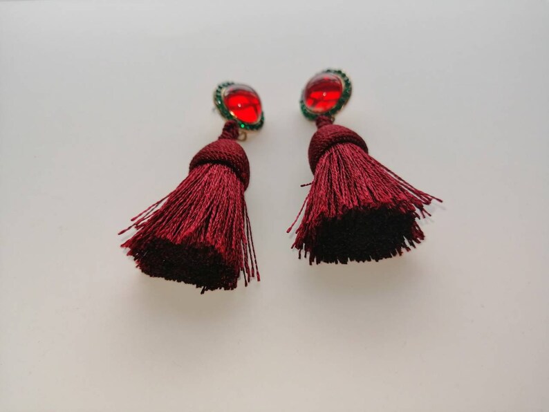 May include: A pair of maroon tassel earrings with red and green gem accents.