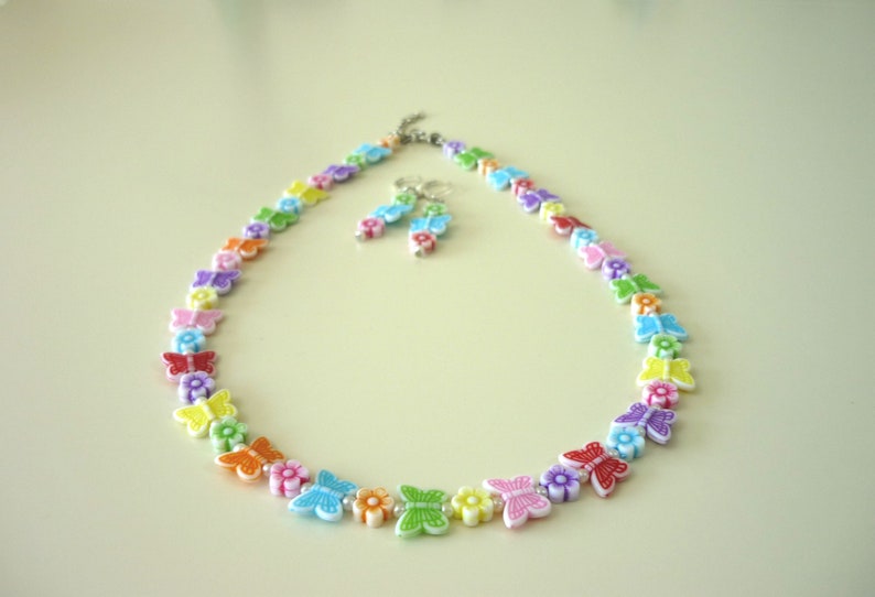 May include: A colorful necklace and matching earrings featuring a rainbow of butterflies with flowers. The necklace is made of plastic beads and is strung on a silver chain.