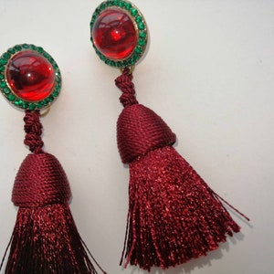 May include: A pair of red tassel earrings with green rhinestone accents. The earrings feature a round red stone surrounded by green rhinestones.