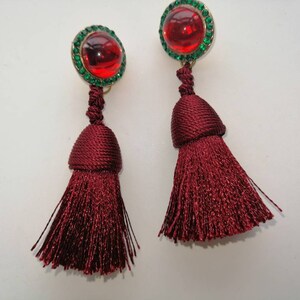 May include: A pair of red tassel earrings with green jeweled tops. The tassels are made of a soft, silky material.