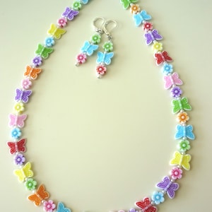 May include: A rainbow colored butterfly necklace and earrings set. The necklace is made of white beads with colorful butterfly charms. The earrings are silver with colorful butterfly charms.