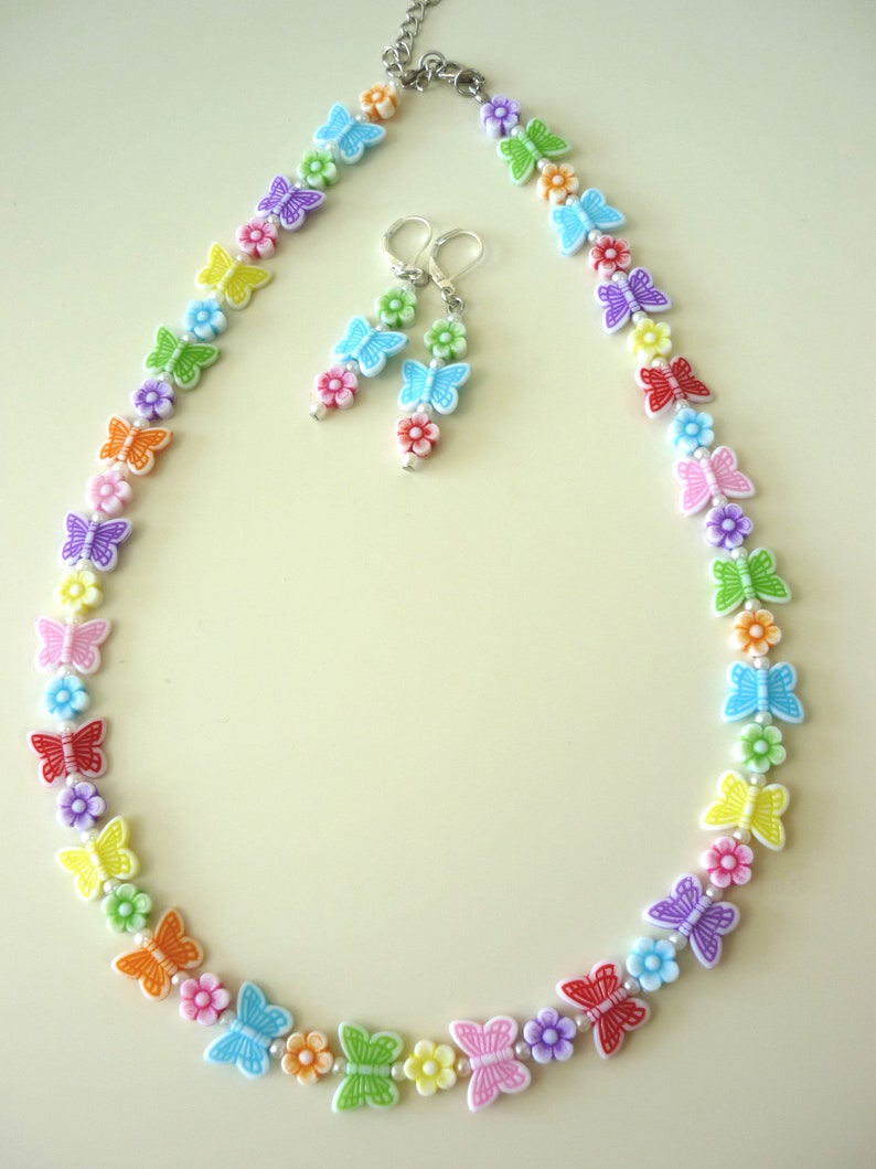 May include: A rainbow colored butterfly necklace and earrings set. The necklace is made of white beads with colorful butterfly charms. The earrings are silver with colorful butterfly charms.