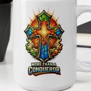 以下が含まれることがあります： 鮮やかな十字架のデザインが施された白いセラミックマグ。背景には放射状の太陽が描かれています。十字架は緑、青、オレンジ色のアクセントで装飾されています。「MORE THAN A CONQUEROR」のテキストが大胆で様式化されたフォントで表示されています。