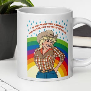Puede incluir: Taza de cerámica blanca con una colorida ilustración de una mujer con sombrero de vaquero y camisa a cuadros, sobre un arcoíris. La taza tiene el texto: "If you want the rainbow you gotta put up with the rain."