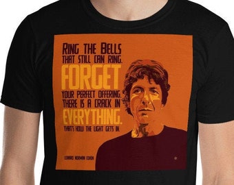 May include: Black t-shirt with an orange and yellow graphic featuring a man's face and the text "RING THE BELLS THAT STILL CAN RING FORGET YOUR PERFECT OFFERING THERE IS A CRACK IN EVERYTHING. THAT'S WHERE THE LIGHT GETS IN."