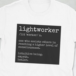 May include: White t-shirt with a black square graphic that defines the word "lightworker" as "one who assists others in reaching a higher level of consciousness. Intuitive being, empath, healer."