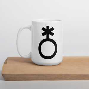 May include: White ceramic mug with a black gender neutral symbol. The symbol is a circle with a cross on top.