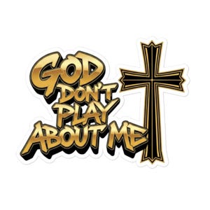 May include: A sticker with the text "GOD DON'T PLAY ABOUT ME" in gold lettering with a black outline. A black cross with gold trim is to the right of the text. The sticker has a white background.