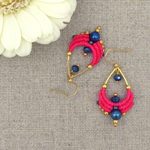 Puede incluir: Un par de pendientes de gota de agua hechos con cuentas rosas y azules con detalles dorados.