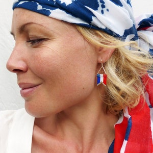 Op de afbeelding: Een vrouw draagt een witte, blauwe en rode gepatroneerde hoofdoek met een zilveren oorbel met een klein Frans vlaggetje.